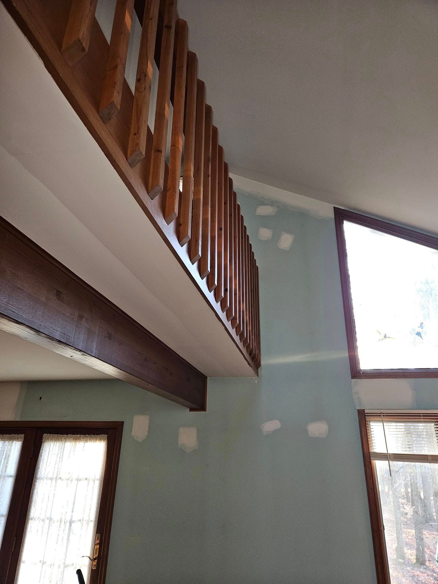 Loft interior with wooden railing, green walls, and large windows letting in daylight