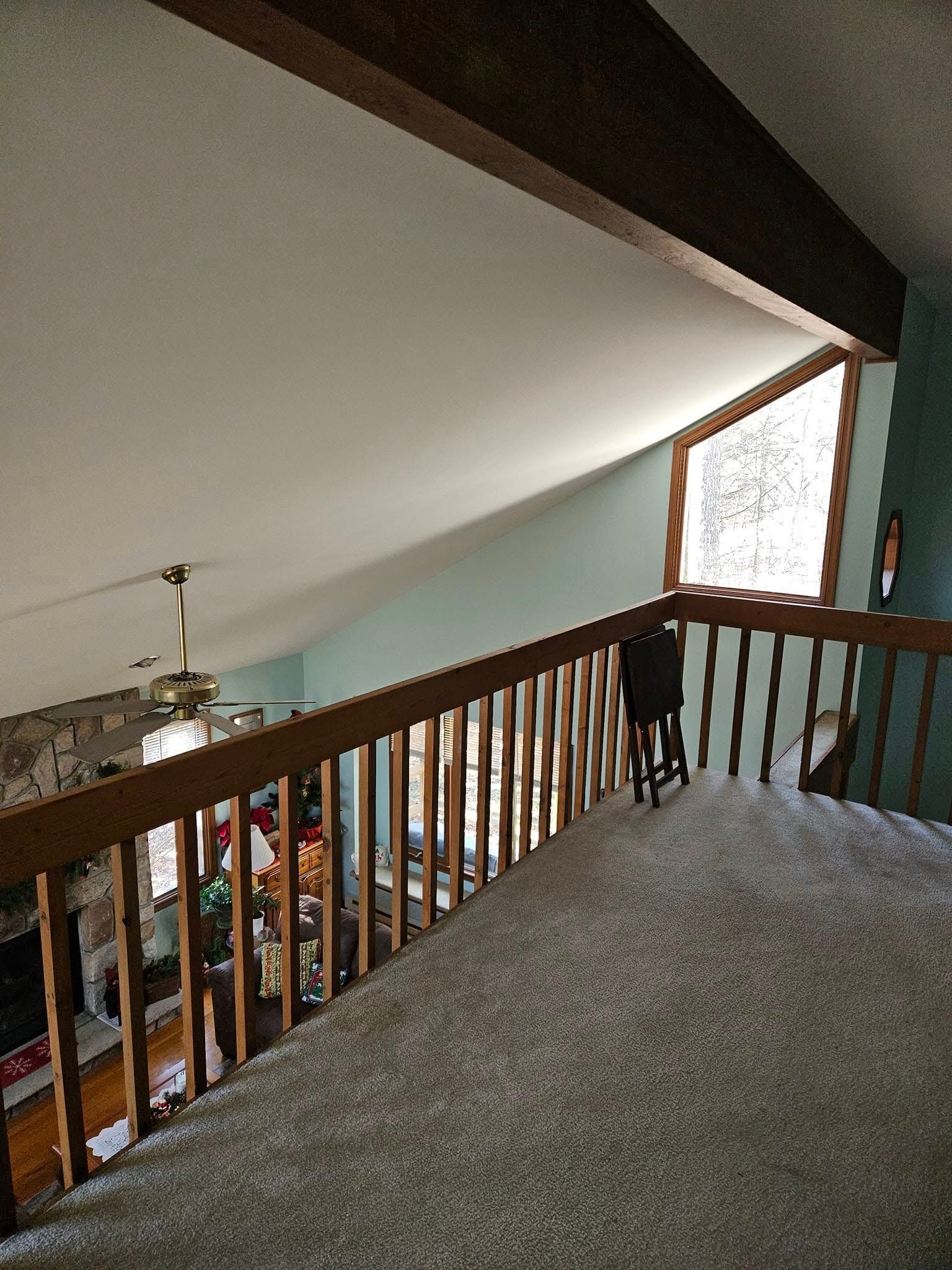 Loft landing with gray carpet, wooden railing, sloped ceiling, and large window.