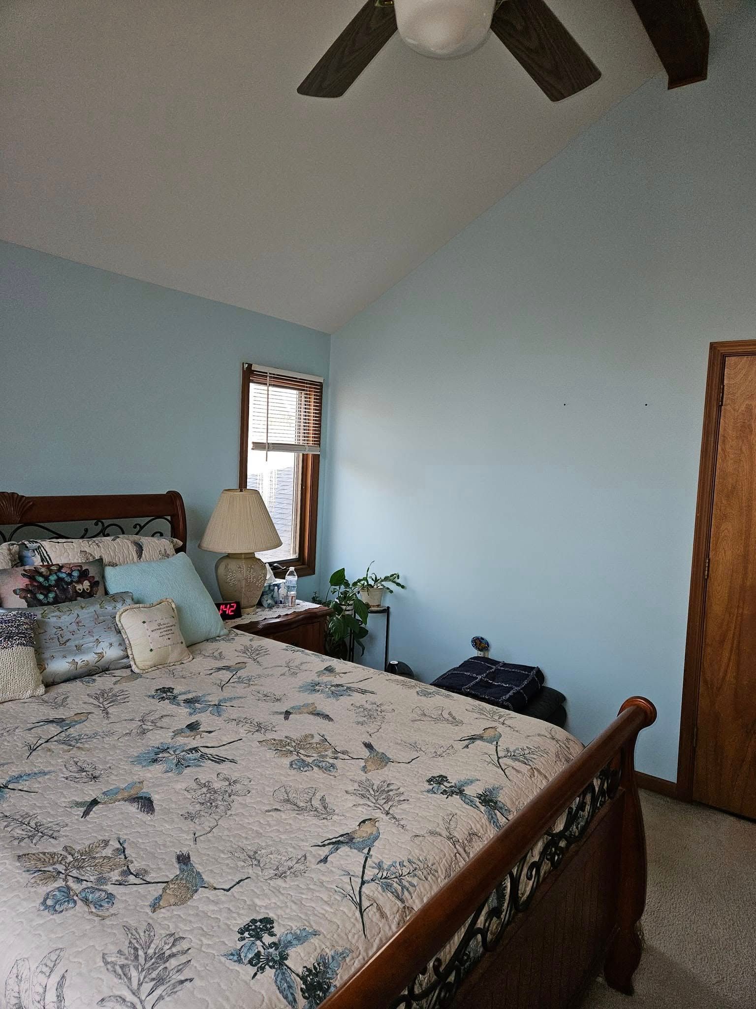 Bedroom with a floral bedspread, light blue walls, wooden furniture, and a ceiling fan.