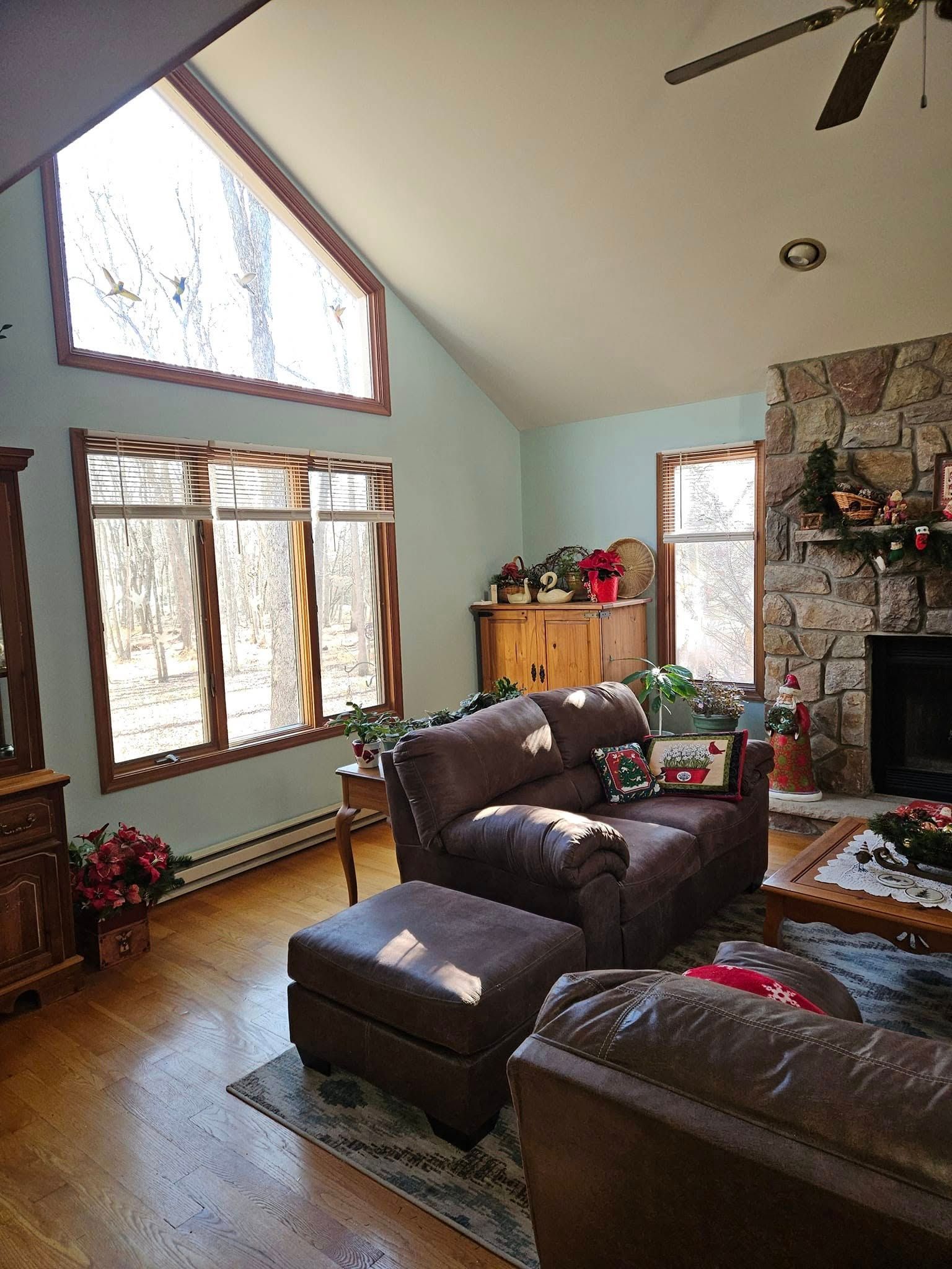 Bright living room with large windows, stone fireplace, leather sofas, and a high vaulted ceiling.