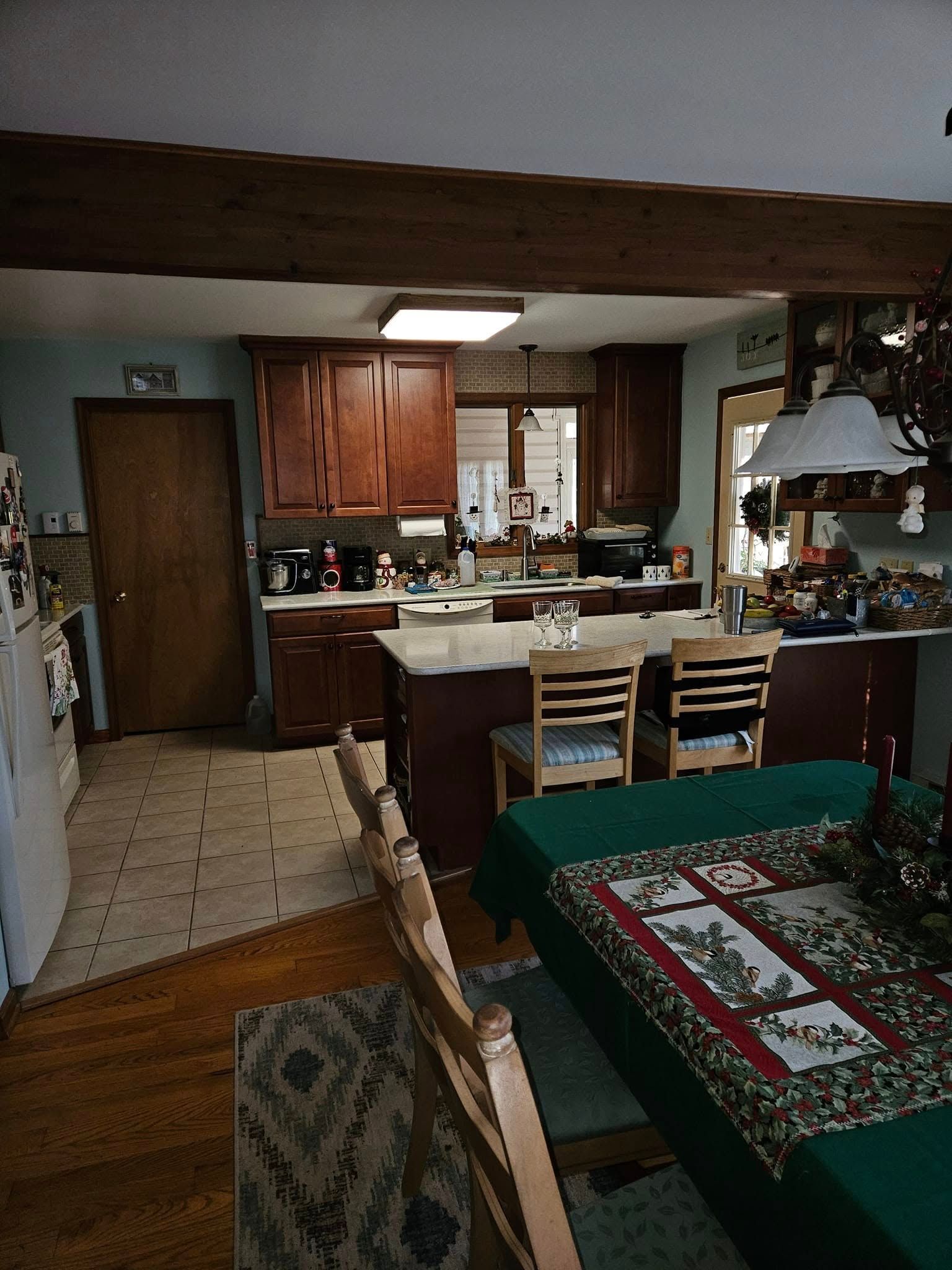 Cozy kitchen and dining area with wooden cabinets, white chairs, and a green tablecloth in the foreground