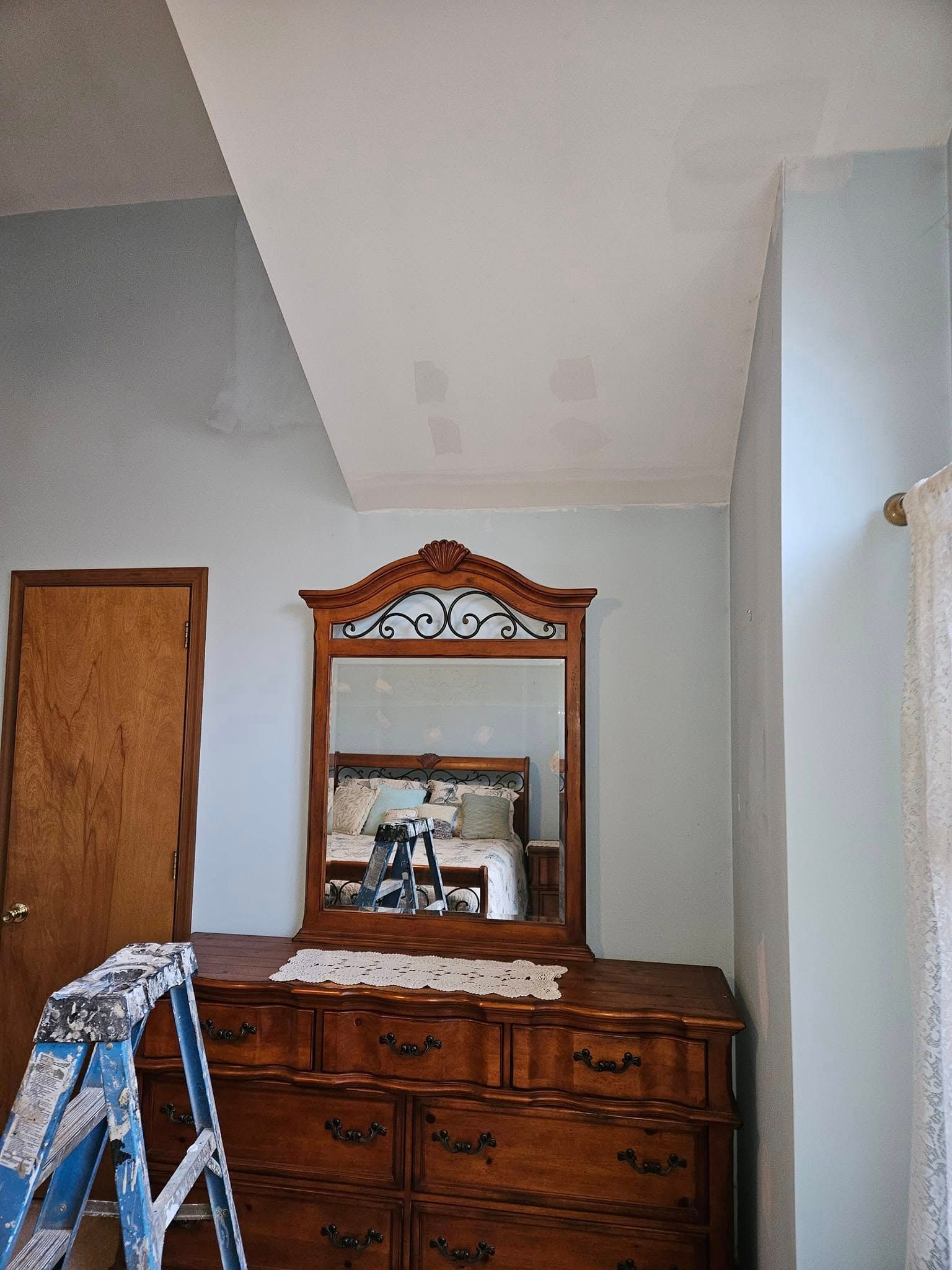 Wooden dresser with mirror in a sparsely furnished room, with a ladder at left and slanted ceiling above.