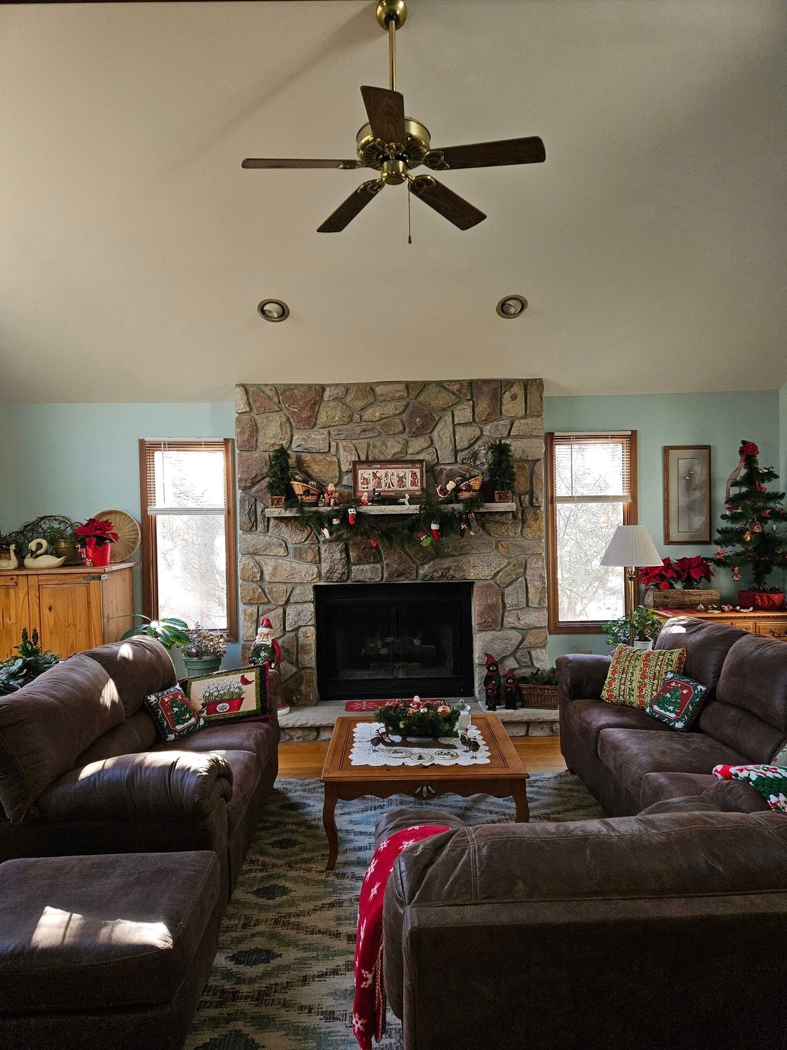 Cozy living room with brown sofas, stone fireplace, coffee table, and ceiling fan