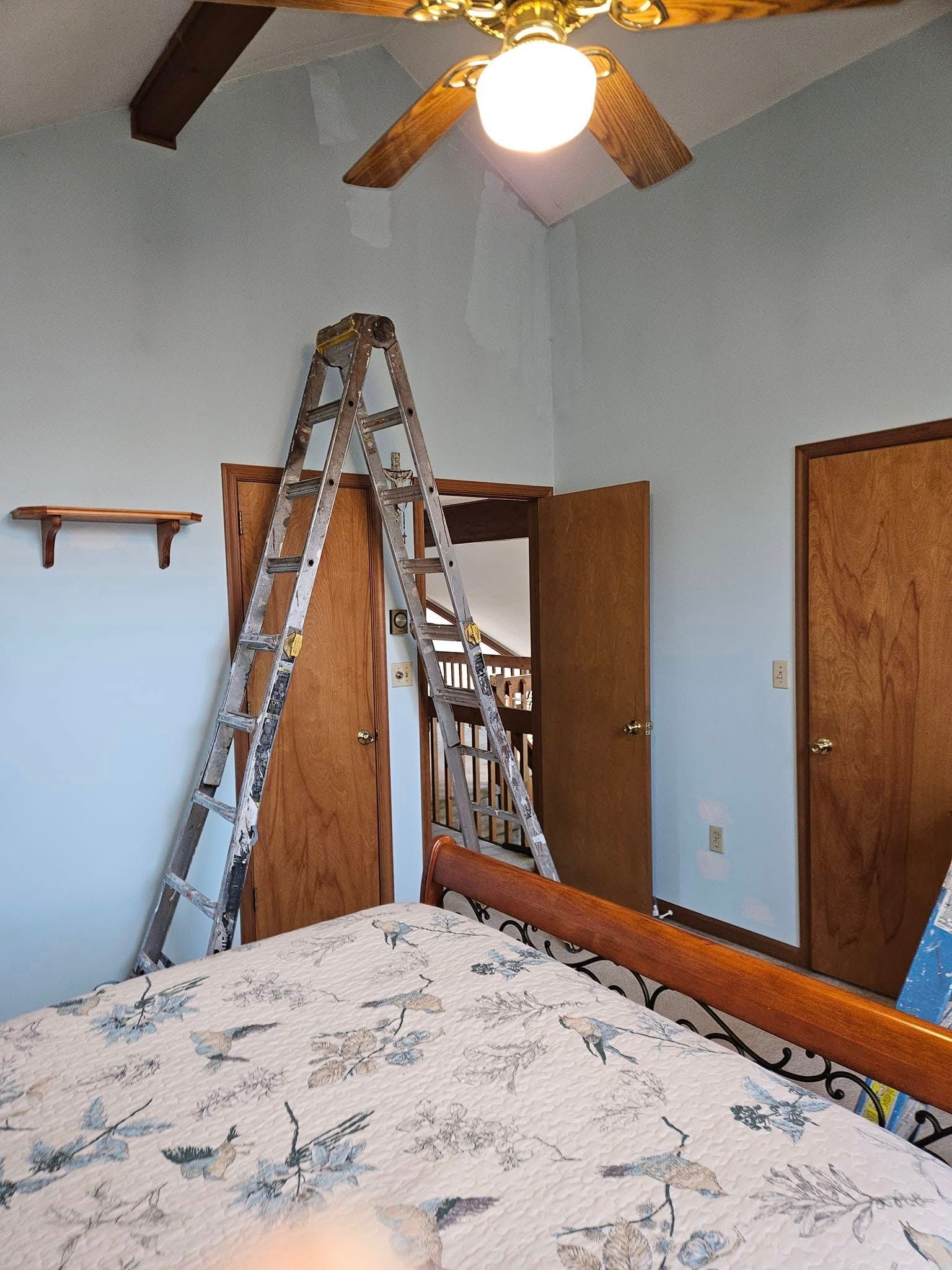 Bedroom with bed, ladders, open closet doors, ceiling fan, and wooden doors.