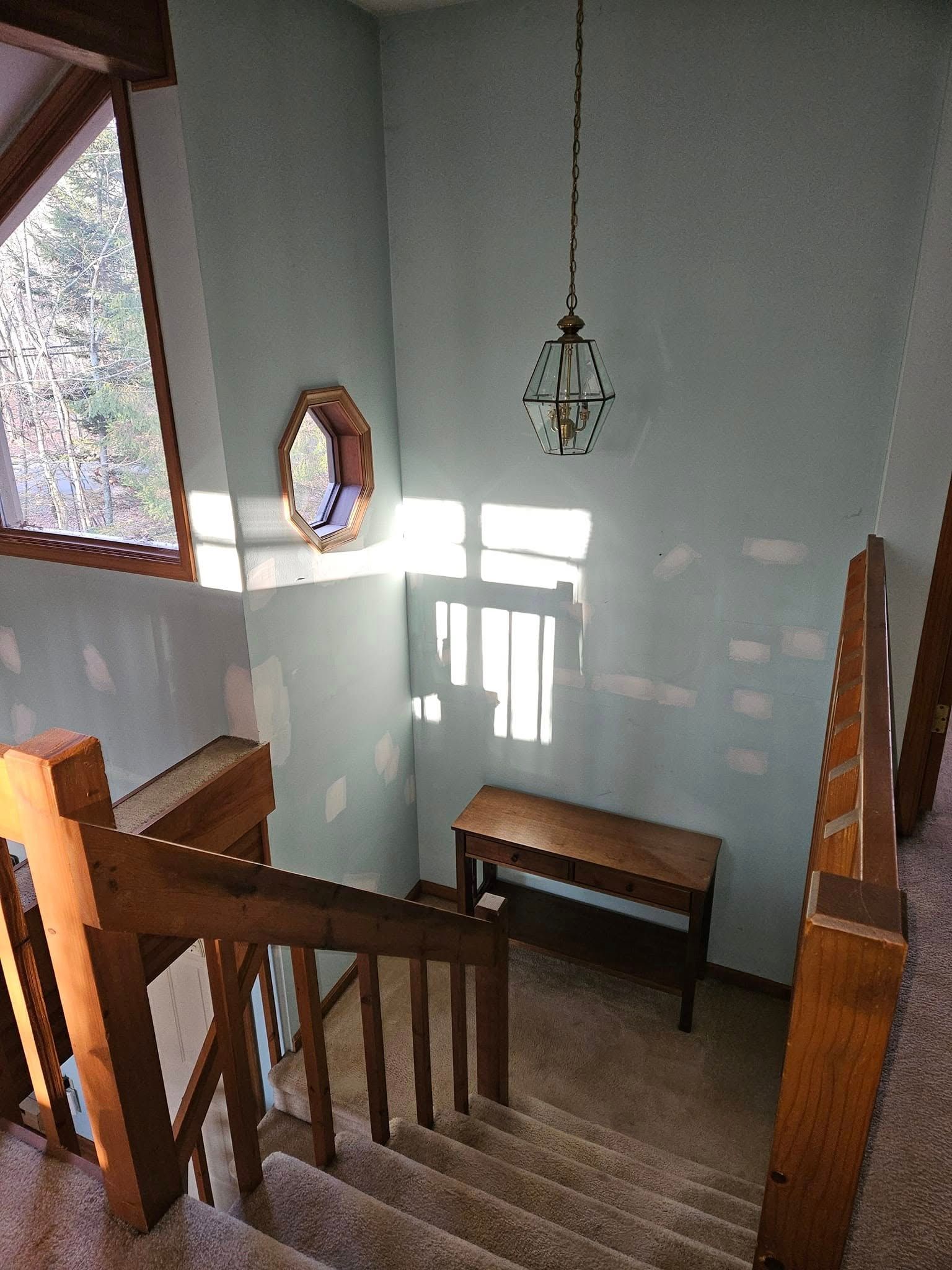 Wooden staircase landing with bench, hanging light, and sunlit wall mirror.