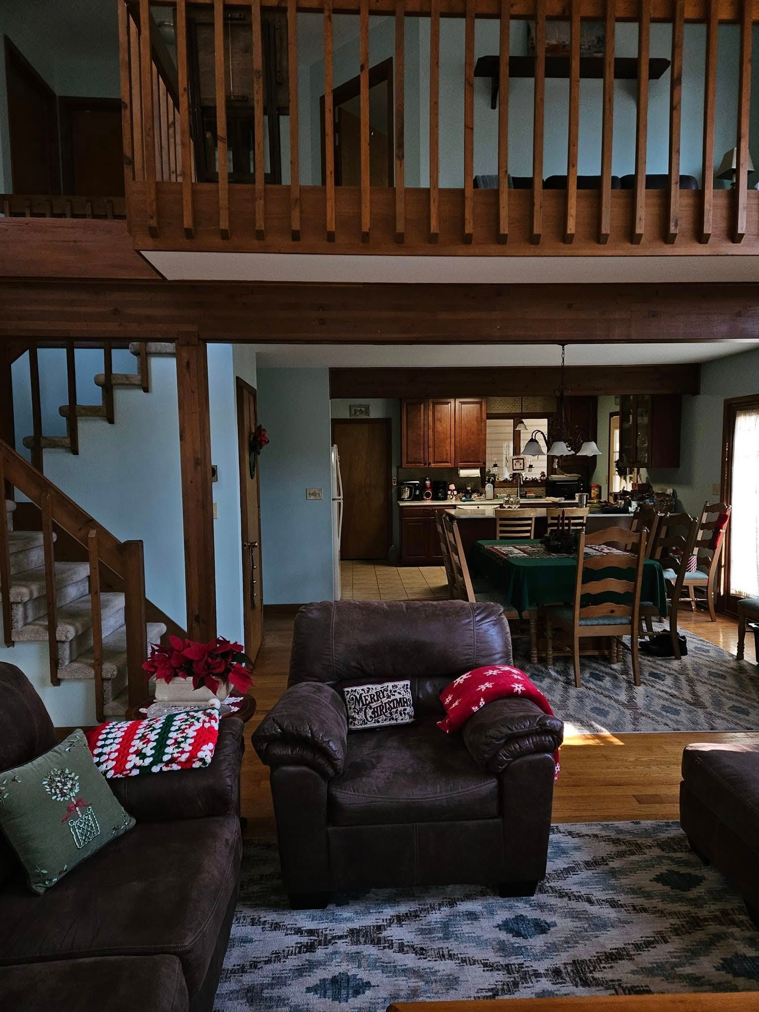 Cozy living room with dark sofas, patterned rug, staircase, and open view to a dining area and kitchen.
