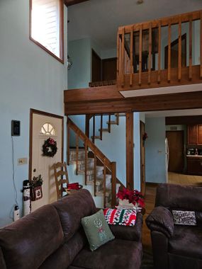 Living room with brown sofas, wooden stairs, and a loft railing in a two-story home