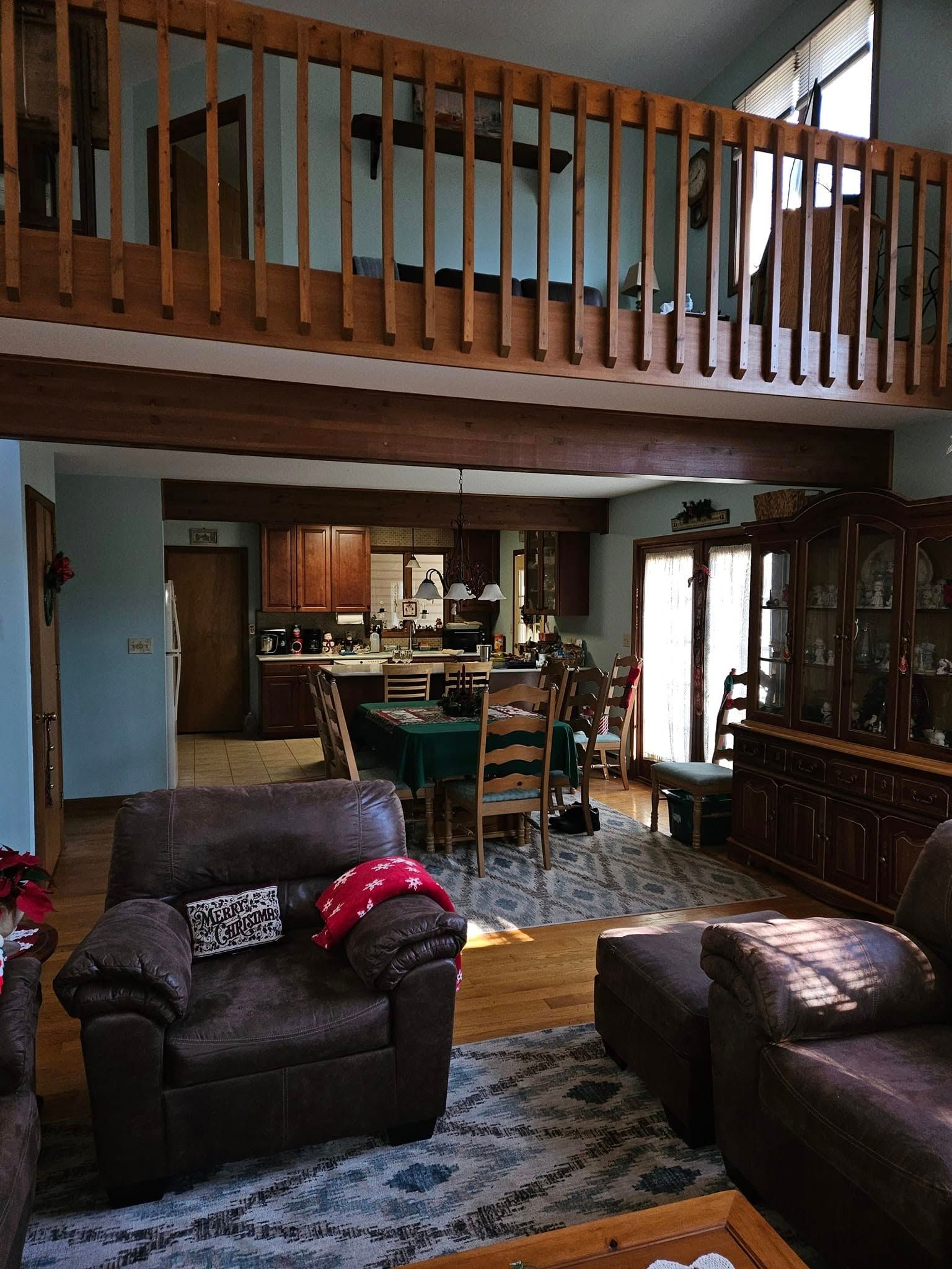 Living room with loft balcony, leather chairs, blue rug, and view into the kitchen and dining area