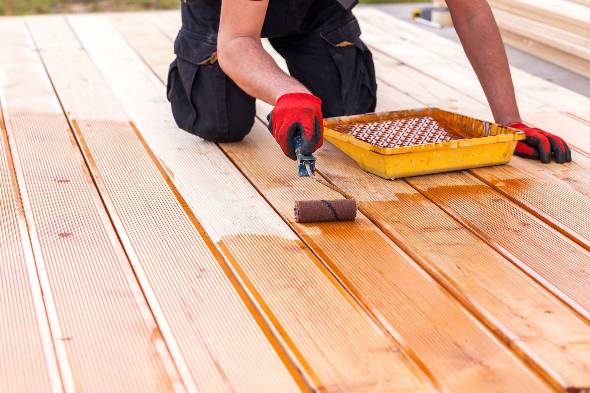 Person staining a wooden deck with a paintbrush and tray of varnish