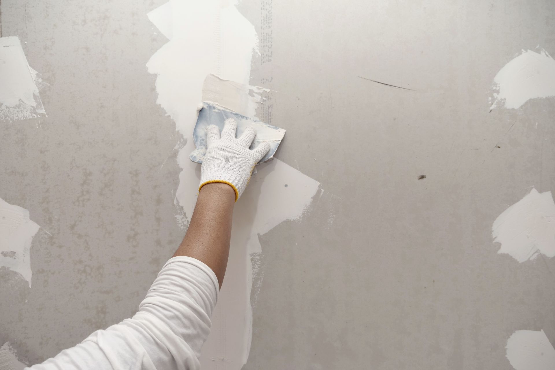 Gloved hand smoothing drywall compound on a wall during patching work