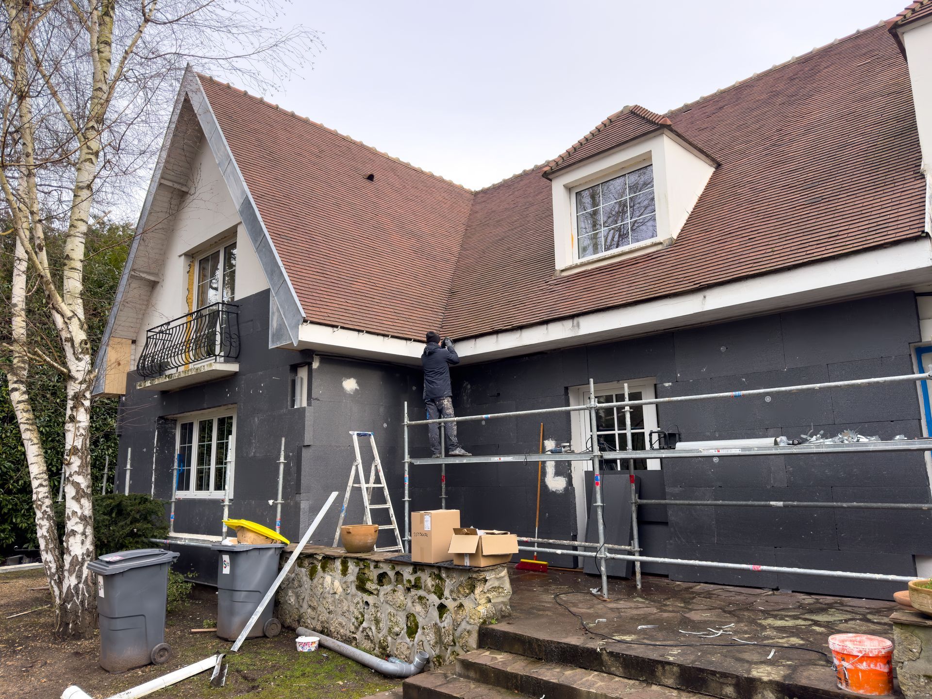 House exterior under renovation with scaffolding, ladders, and construction materials along the wall