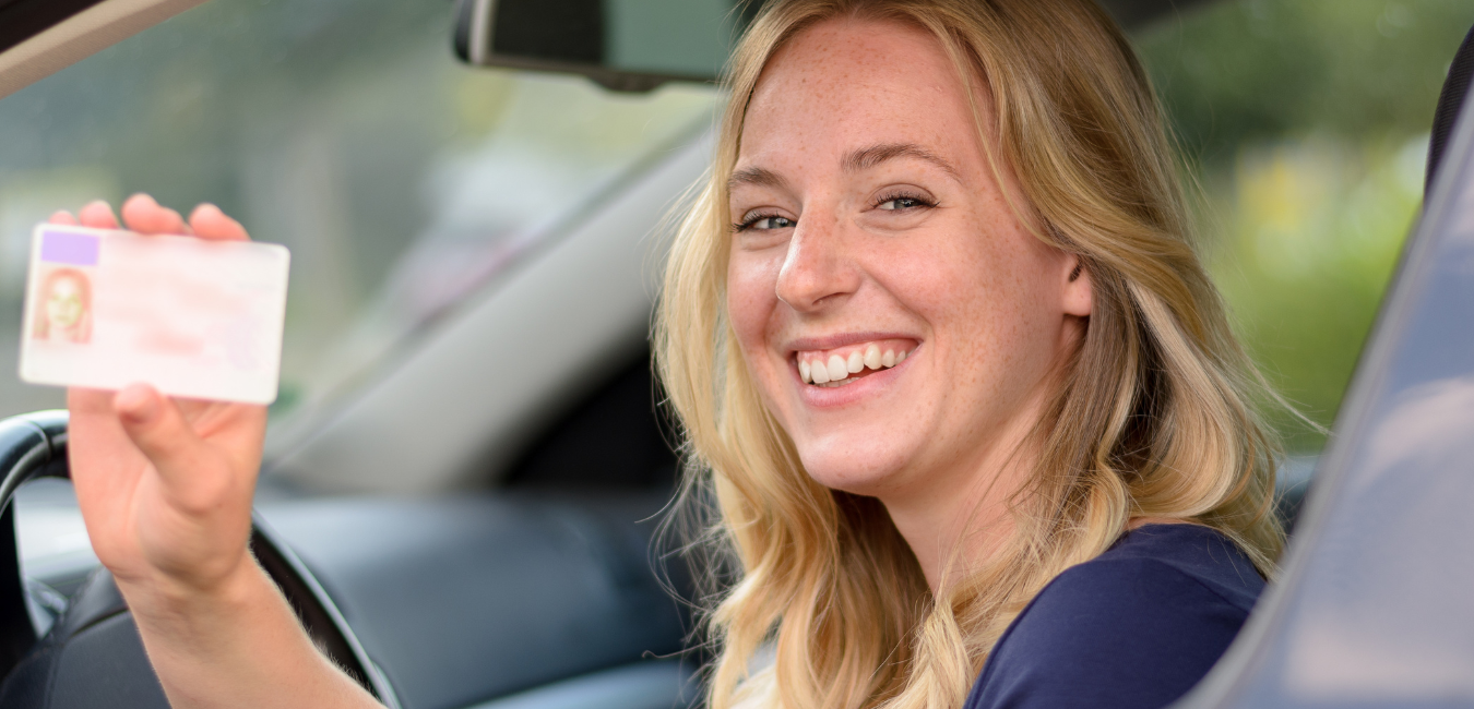 a woman is sitting in a car holding a driving license .