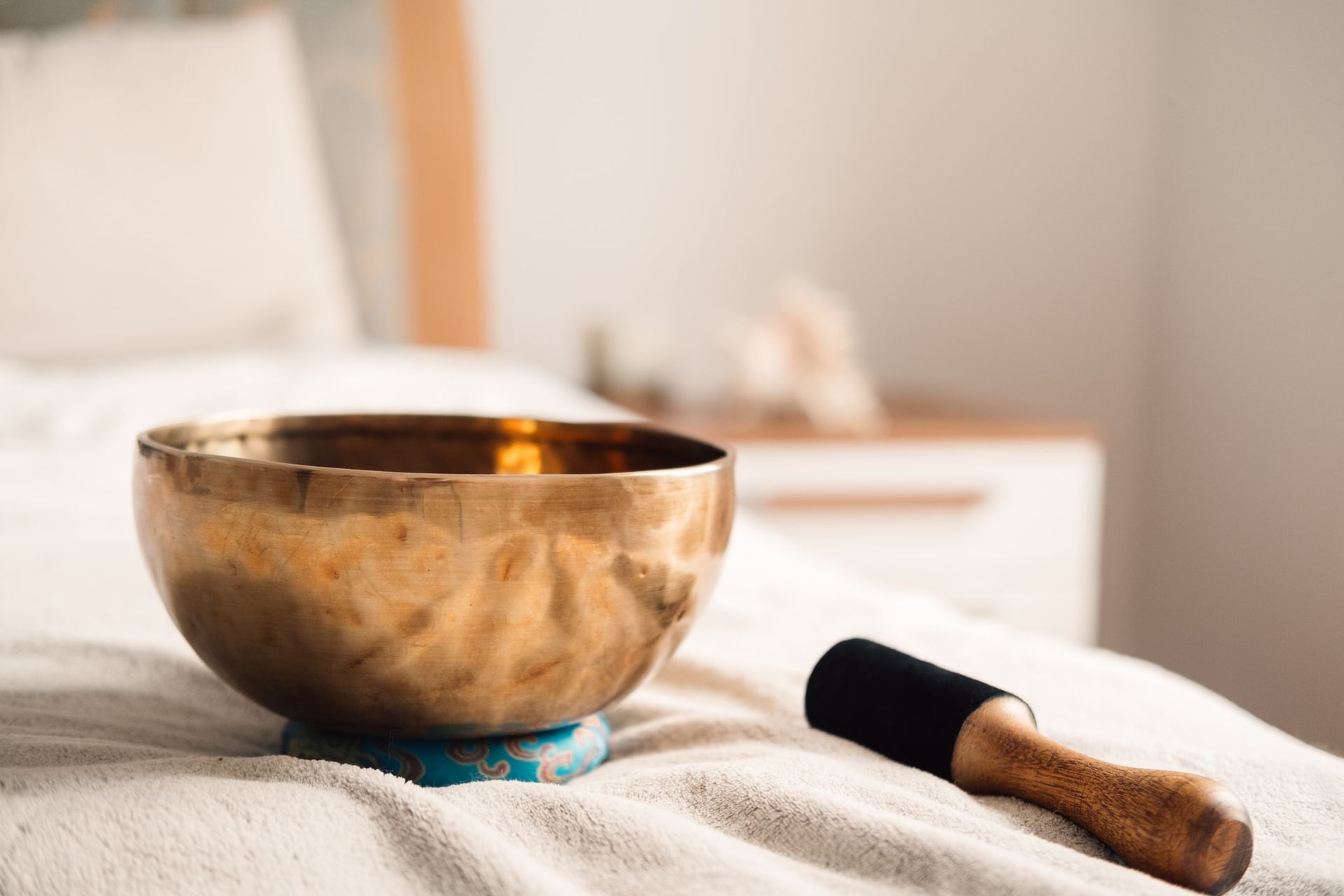 Golden singing bowl and mallet on a bed, used for sound healing.