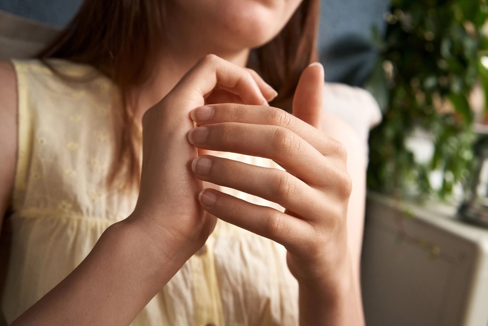 A woman in a yellow shirt is holding her hands together.