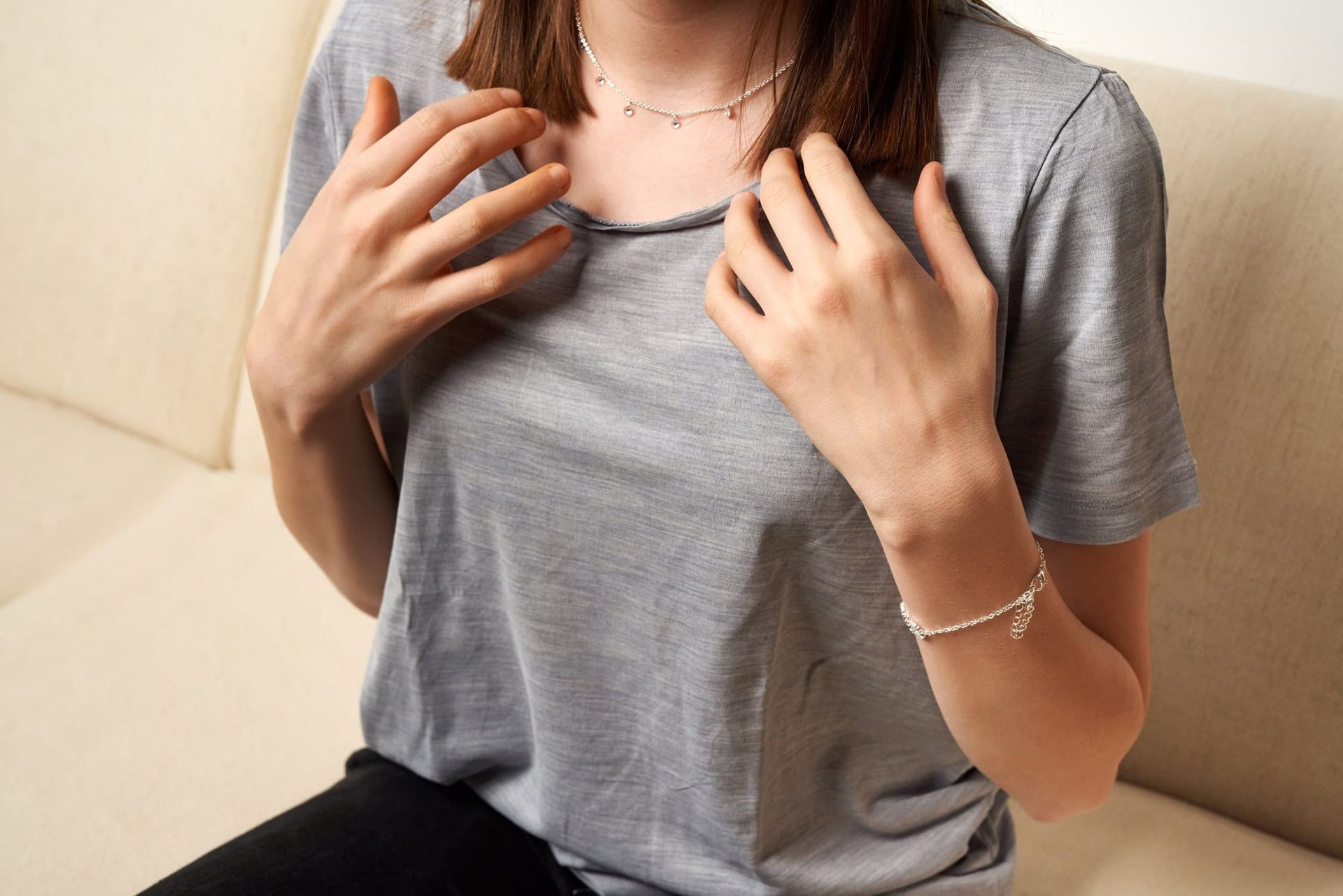 A woman wearing a necklace and a bracelet is sitting on a couch.