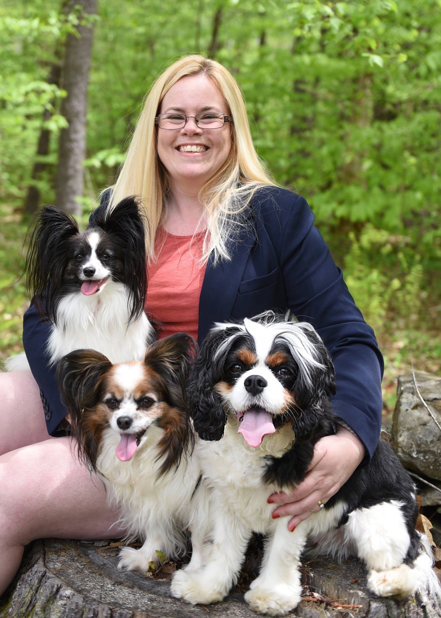 A woman is sitting on a tree stump with three dogs.