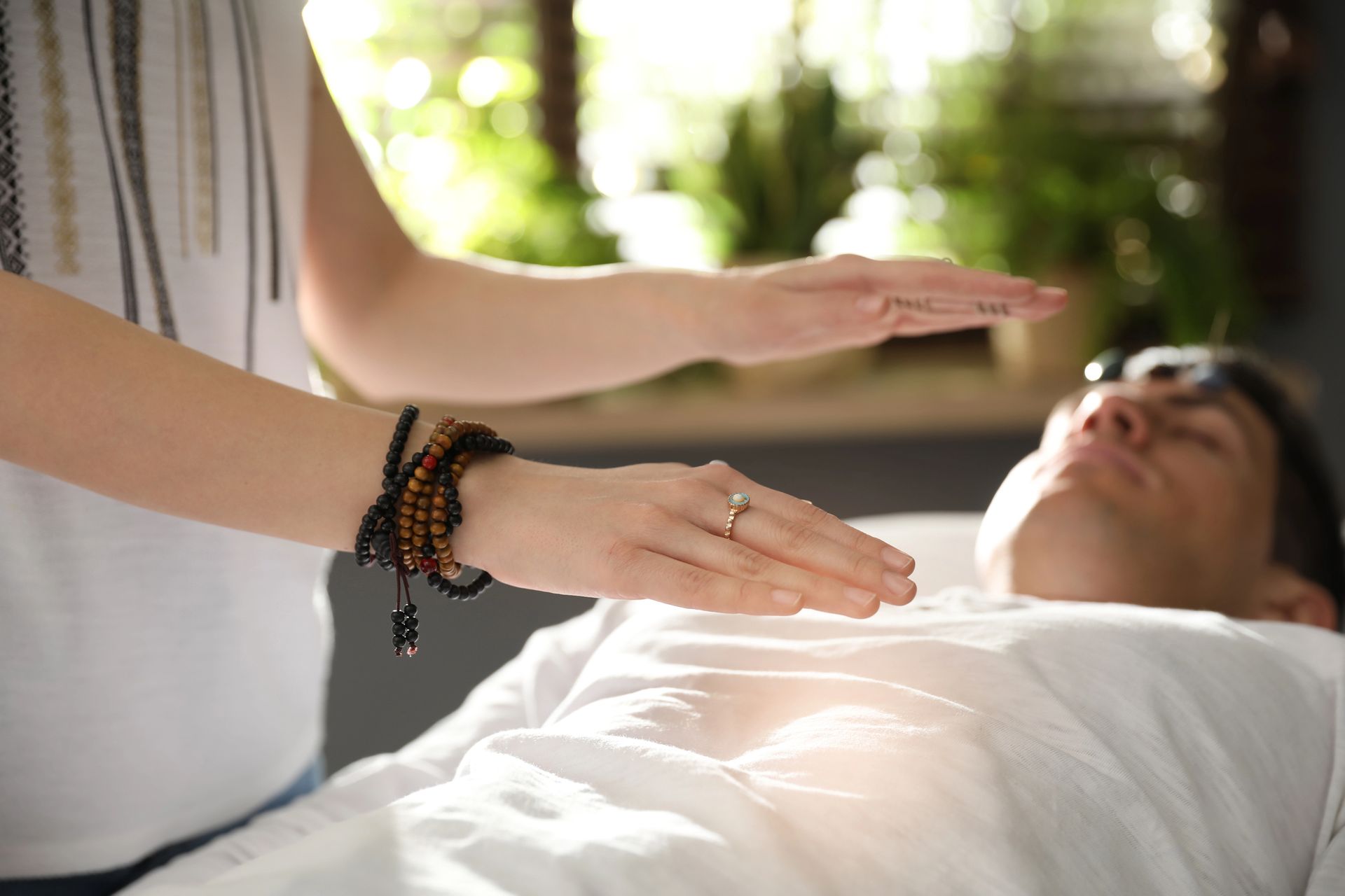 A man is laying on a bed getting a healing session from a woman.