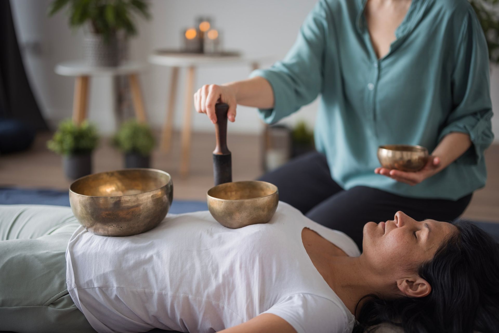 Woman receiving sound therapy: bronze bowls on chest, therapist using mallet.