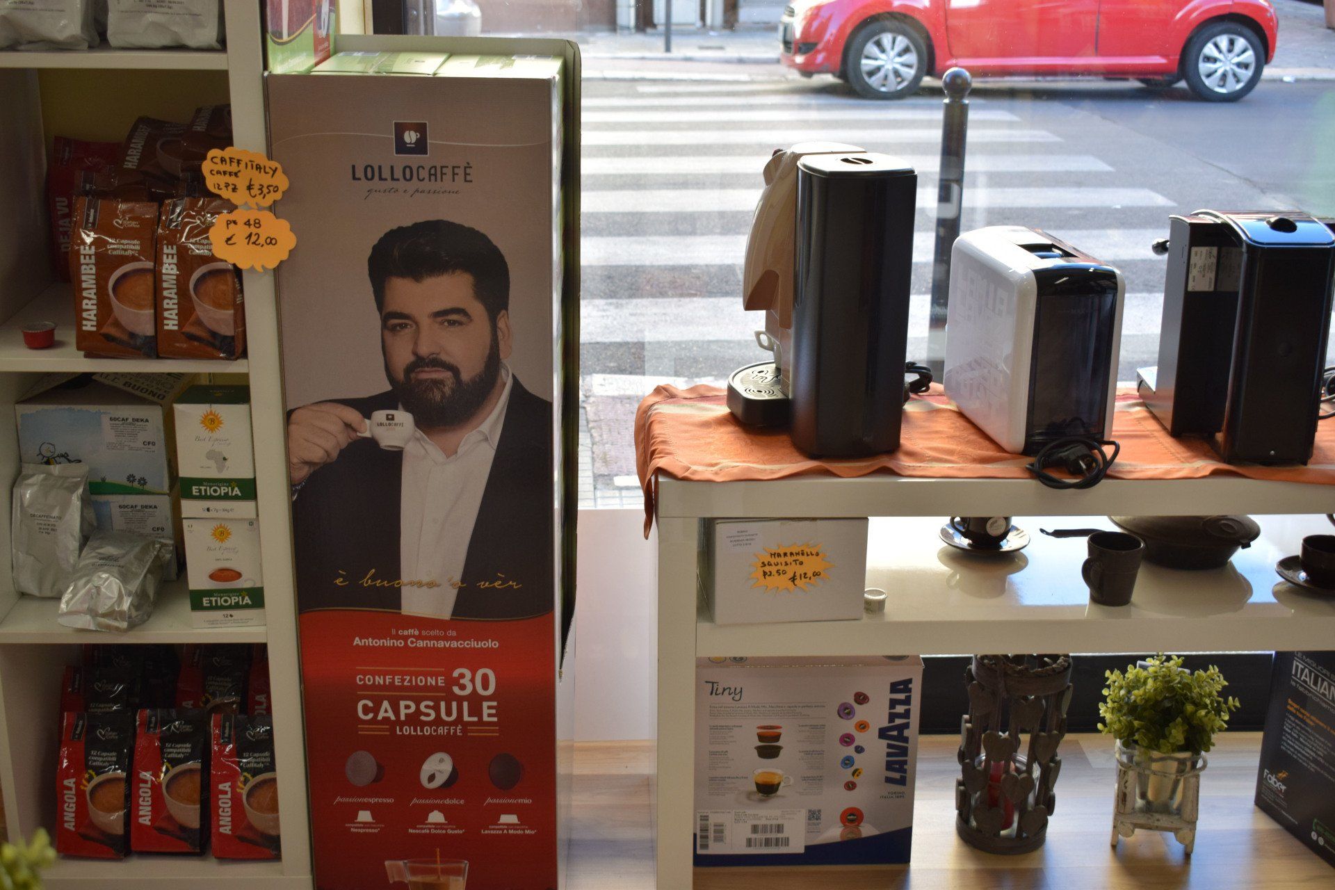 Espositore da bar con macchine per caffè espresso, capsule e un poster di un uomo che gusta un caffè.