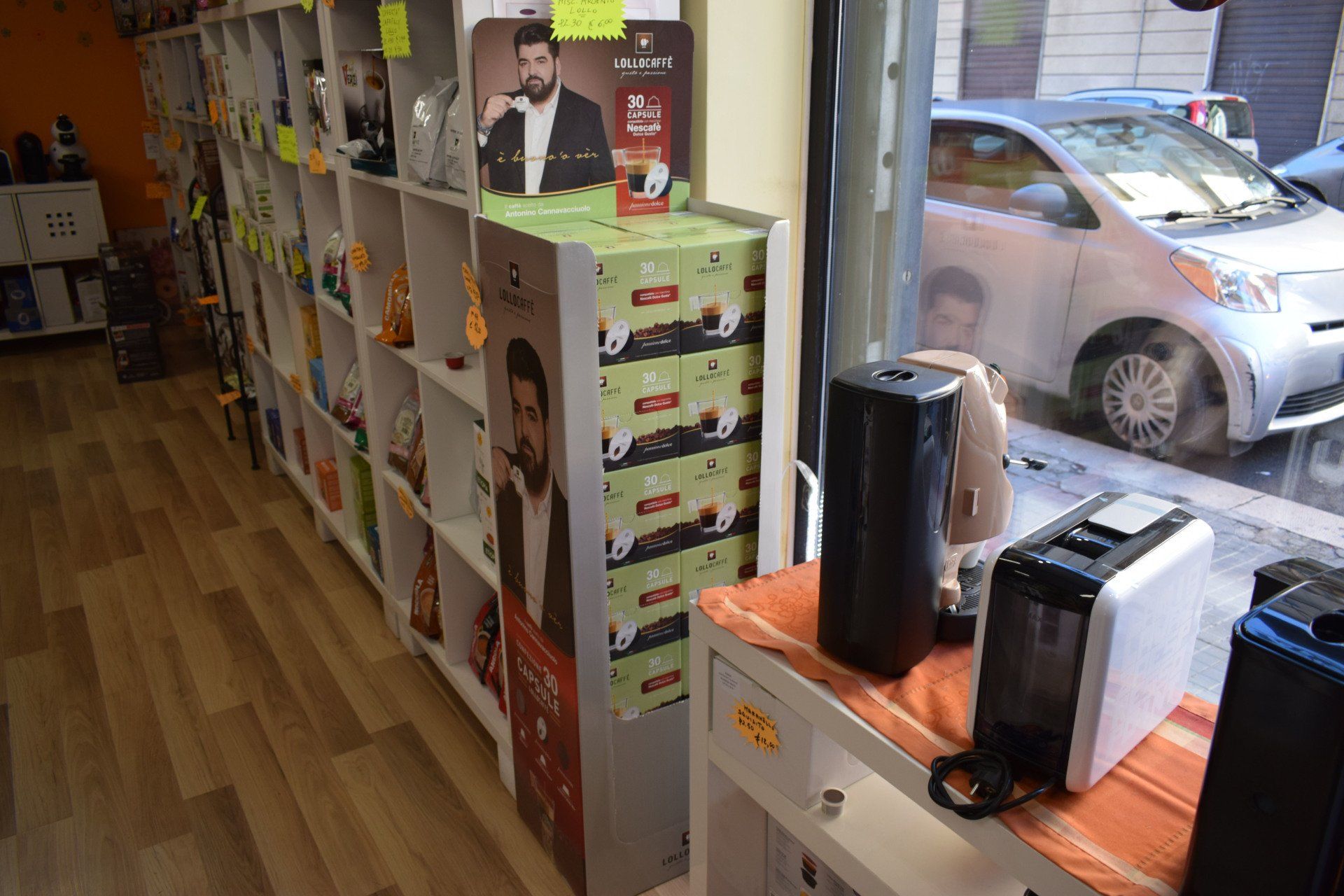 Scaffali di prodotti da caffè e una macchina nella vetrina di un negozio, accanto a un'auto parcheggiata.