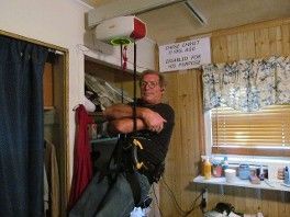 Man in a harness exercising indoors near a window and pull-up bar