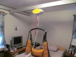 Bedroom with a ceiling-mounted lift and sling chair over a bed.