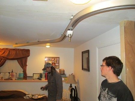 Two people in a living room looking up at a curved ceiling track with a hanging light fixture.