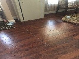 Wooden floor in a room with a cabinet, chair, and pet bed near a window.