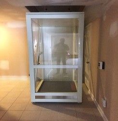 Elevator with white frame in a hallway, reflecting a person inside the cab.