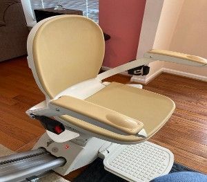 Beige recliner-style stairlift with folded footrest on a wooden staircase