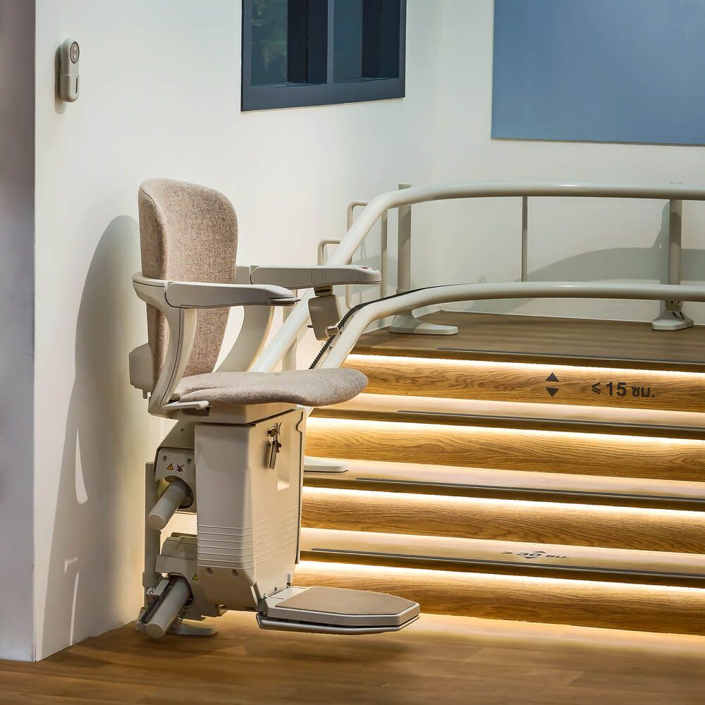 Accessible stair lift chair beside indoor stairs with warm wood steps and a white wall