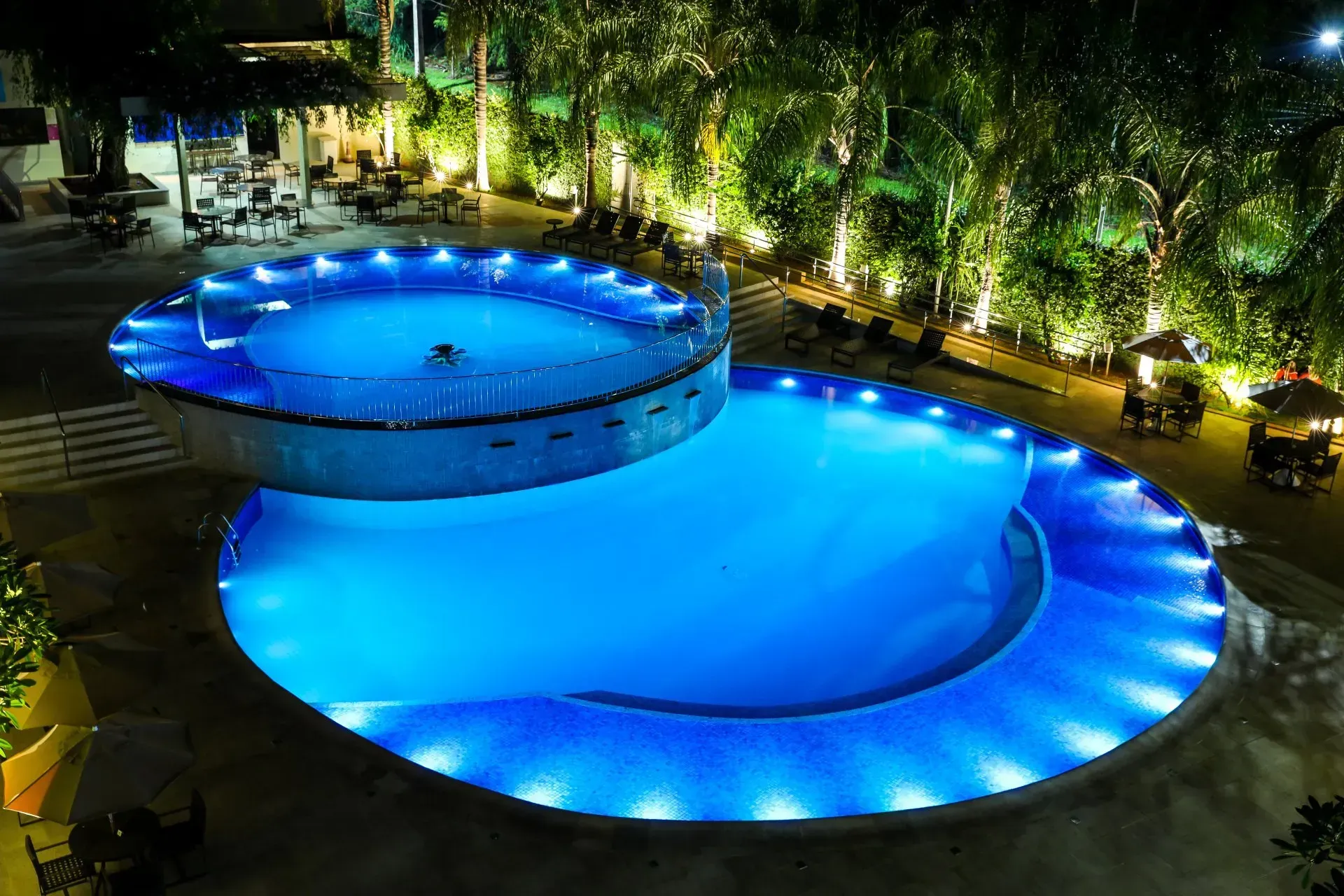 Piscina iluminada à noite com seções circulares. Luzes azuis e árvores.