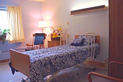 Hospital room with bed, bedside table, armchair, and window with curtains.
