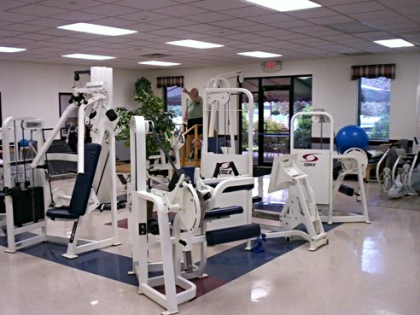 Gym with weight machines and a person using one, bright interior.