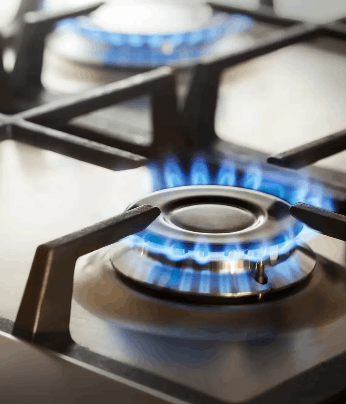 Close-up of a gas stove burner with blue flames on a metal cooktop