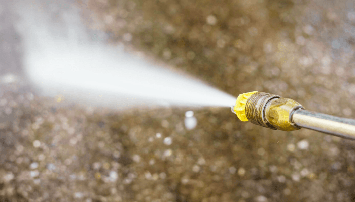 Pressure washer spraying water onto a dirty concrete surface.