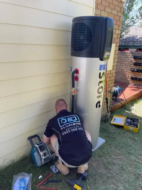 Technician repairing a white outdoor HVAC unit beside a house wall.
