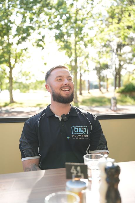 Man smiling at an outdoor café table with trees in the sunlit background