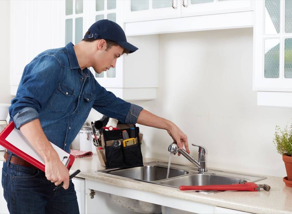 Person using a wrench to fix a kitchen sink faucet with a toolbox nearby