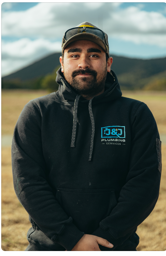 Person in a black hoodie stands outdoors with mountains and cloudy sky in the background