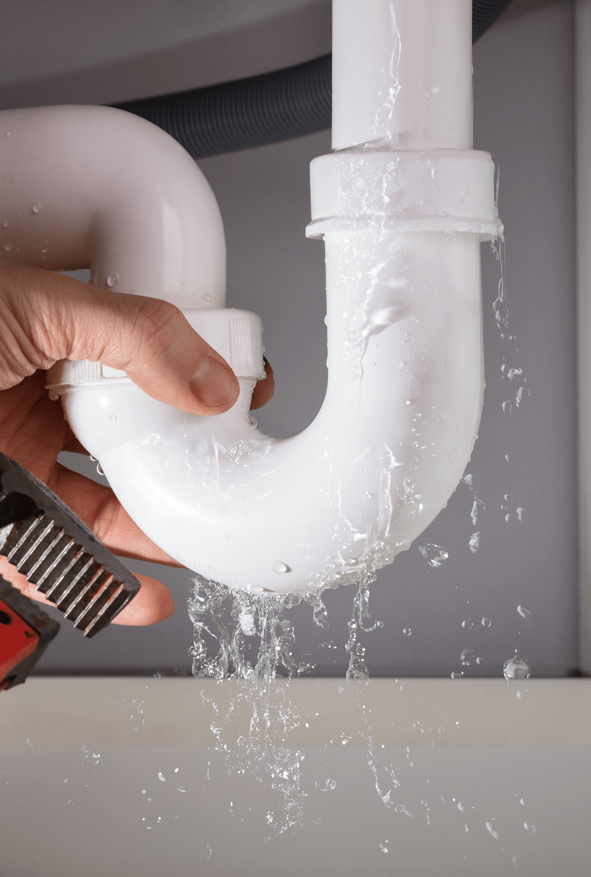 Hand tightening a white PVC pipe under a sink with water leaking from the joint