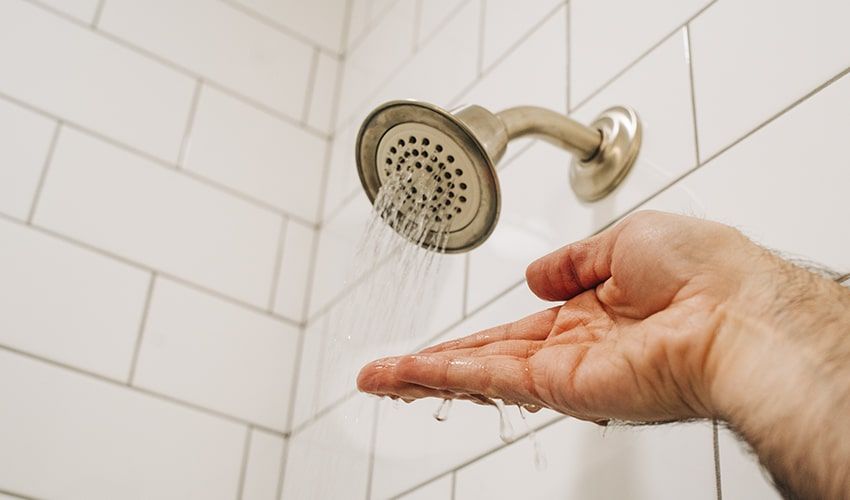 Hand under running showerhead catching water in a white-tiled shower.