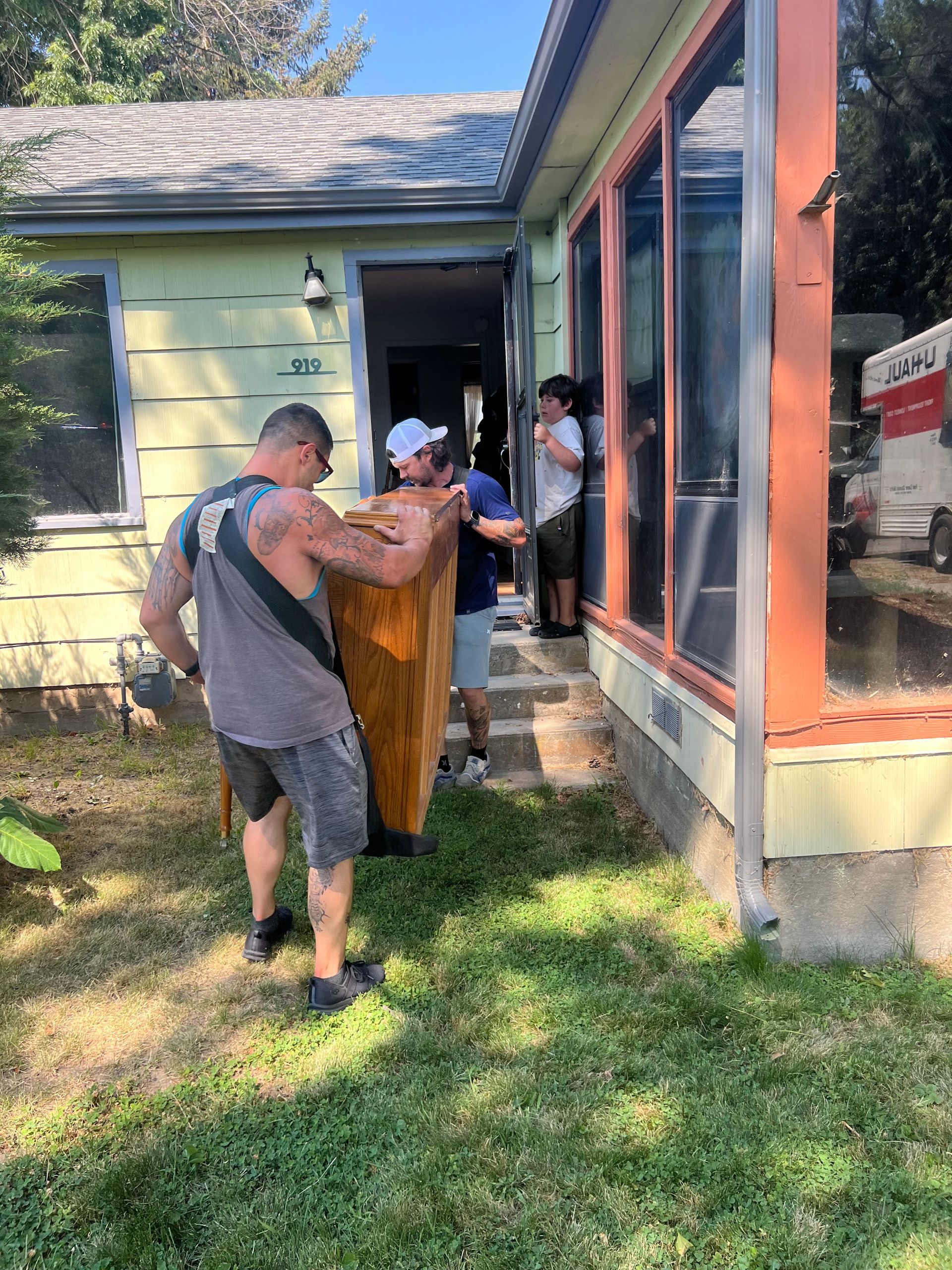 People carrying a large wooden object, possibly a door, into a house with large windows.