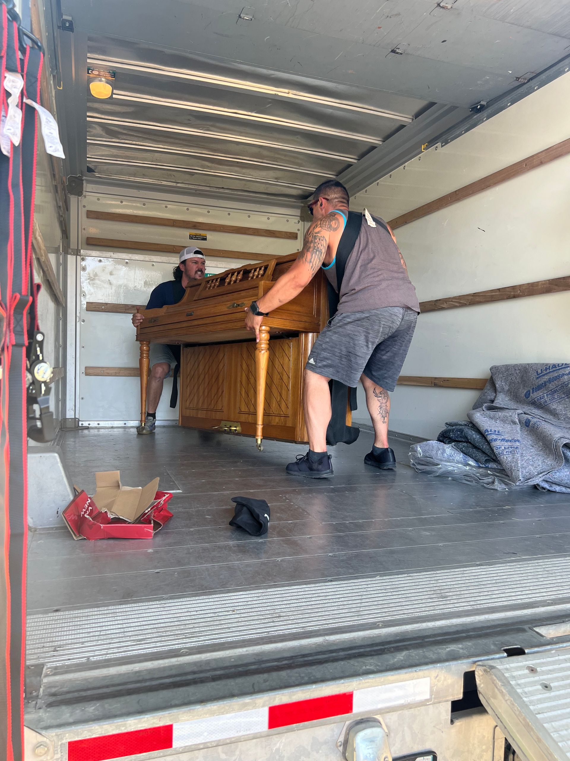 Two people loading a piano into a truck. The men lift a wooden piano.