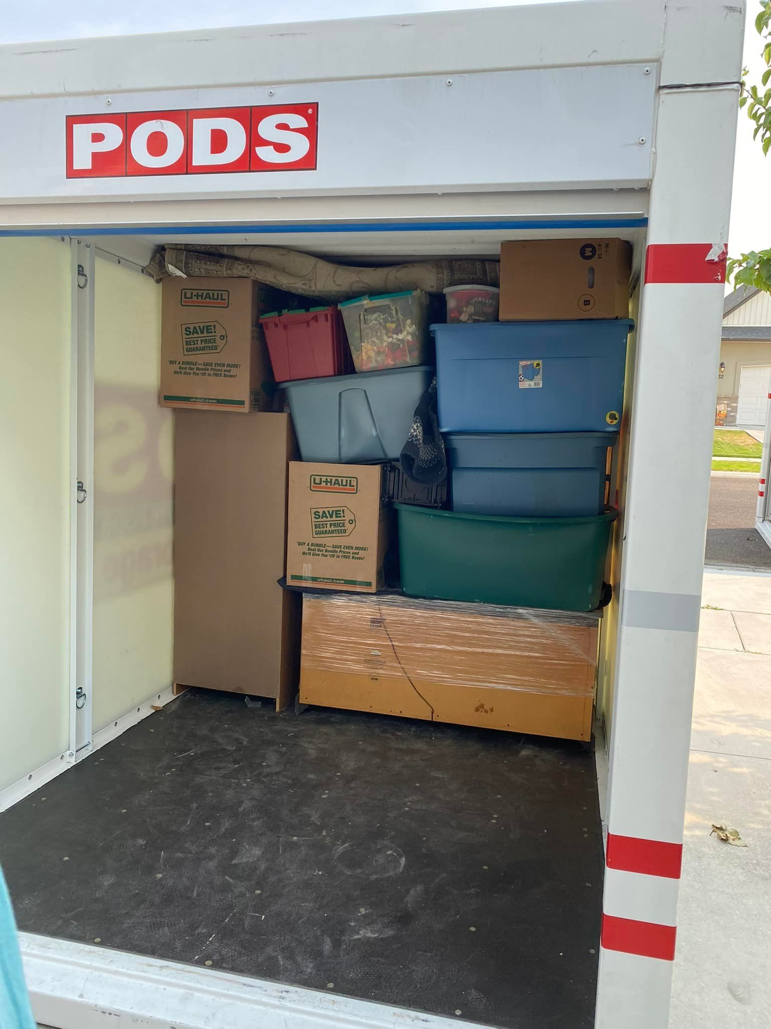A PODS storage container filled with boxes and containers, open, against a residential backdrop.