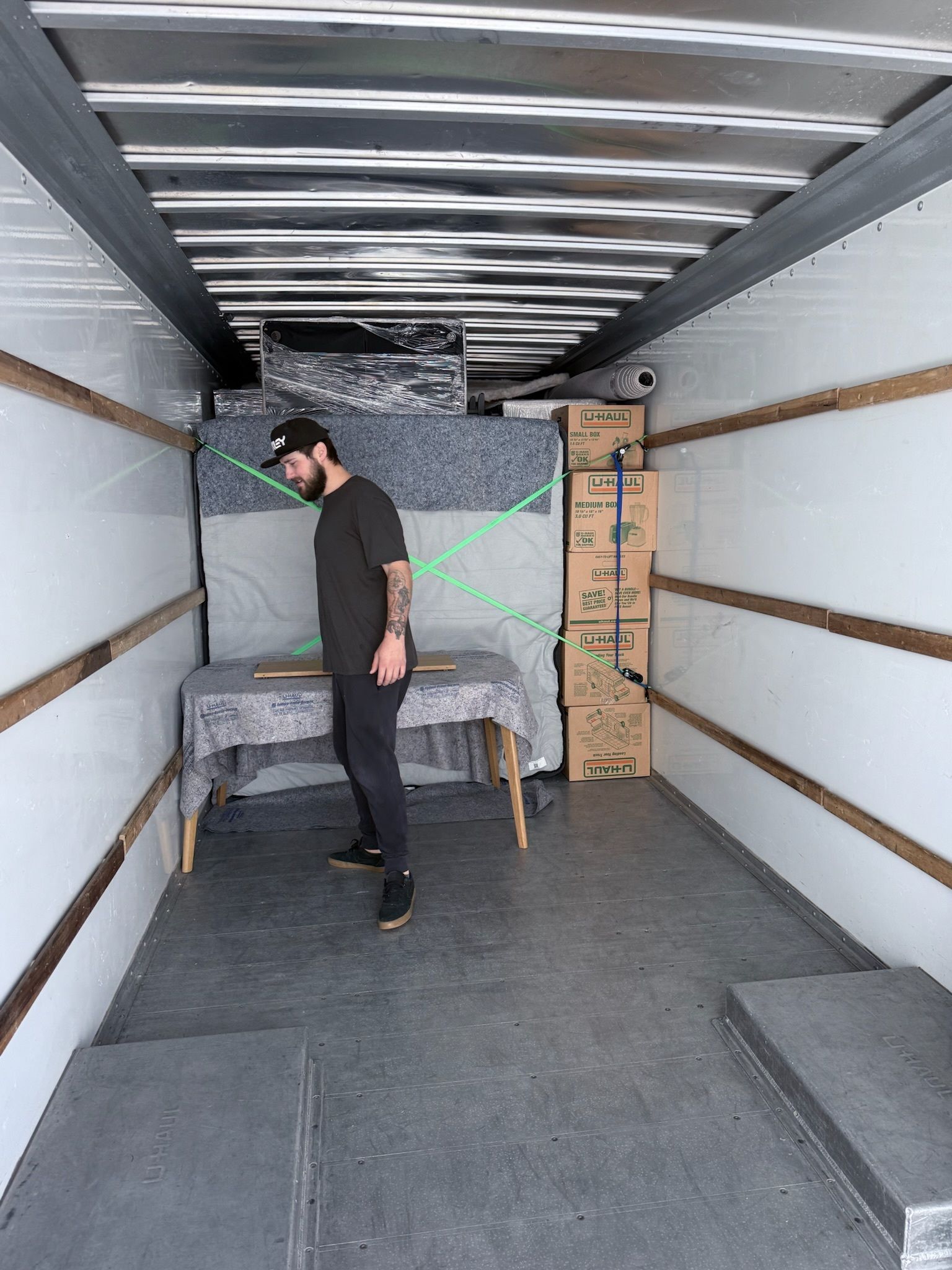 Man standing in a mostly empty moving truck, surrounded by furniture and boxes.