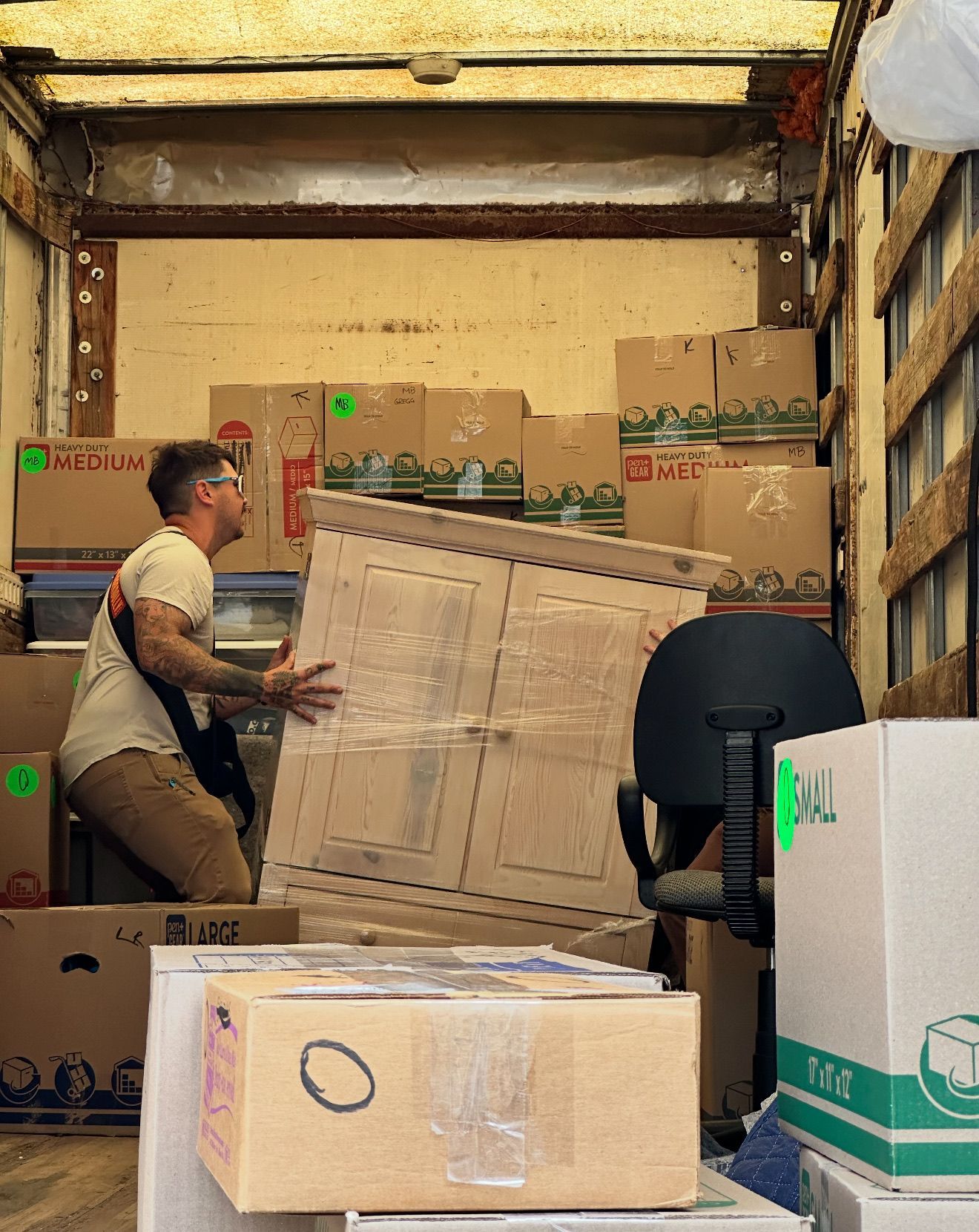 Office space with cardboard boxes, chairs, and wrapped cabinet; moving.