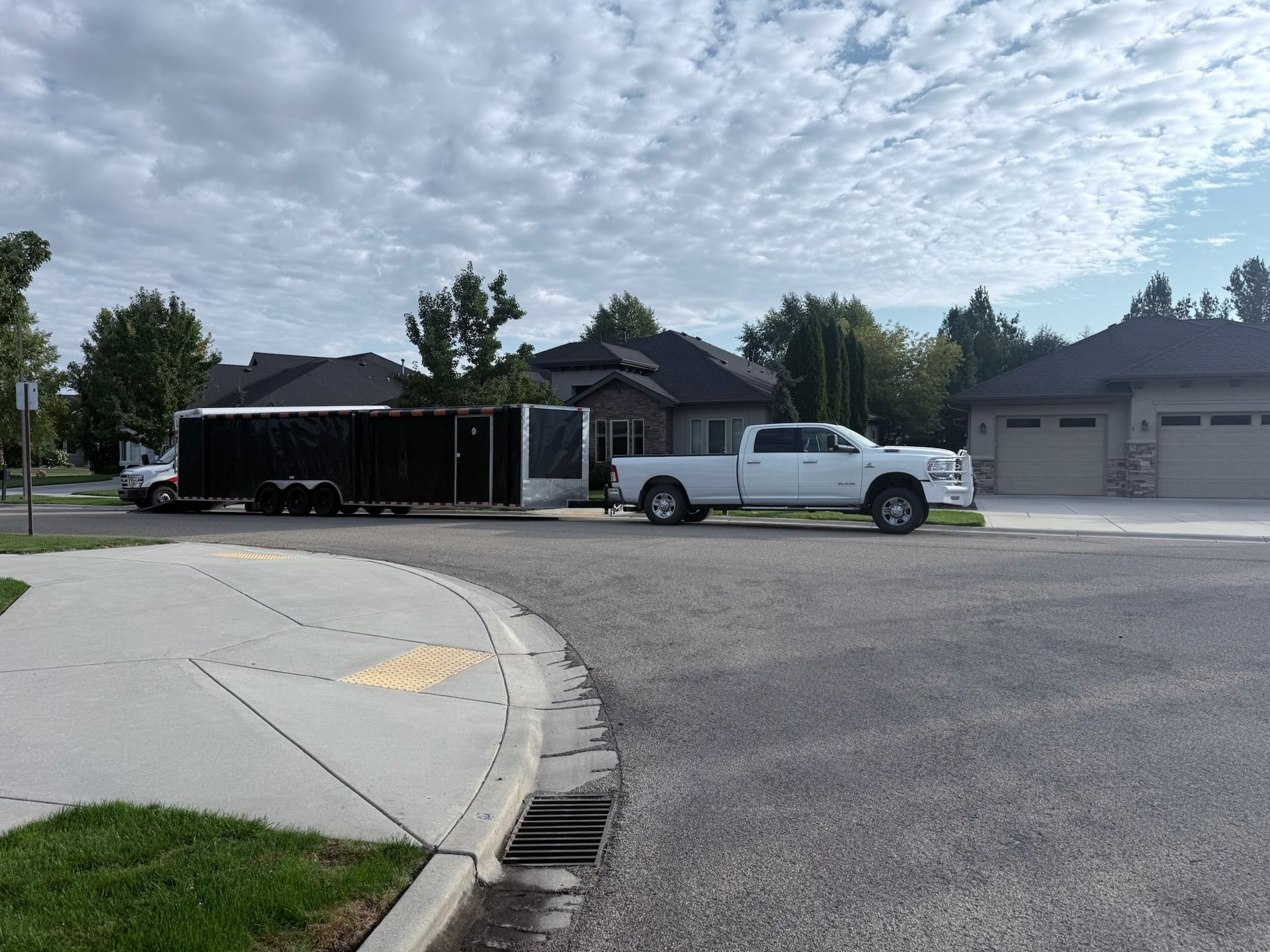 White truck towing a black trailer in a residential area on a cloudy day.