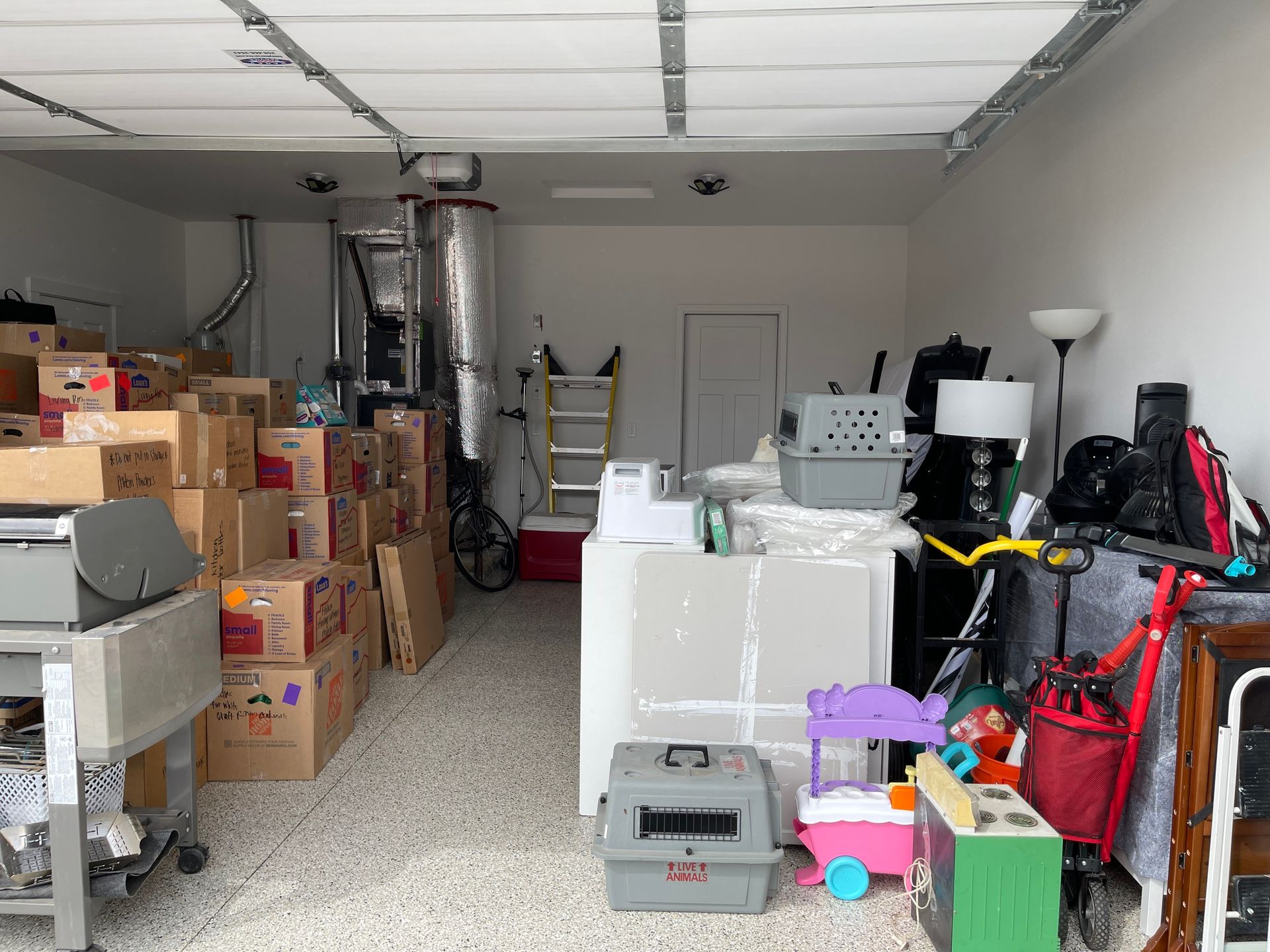 Cluttered garage filled with boxes, furniture, and various items. Interior shot, overhead lighting.