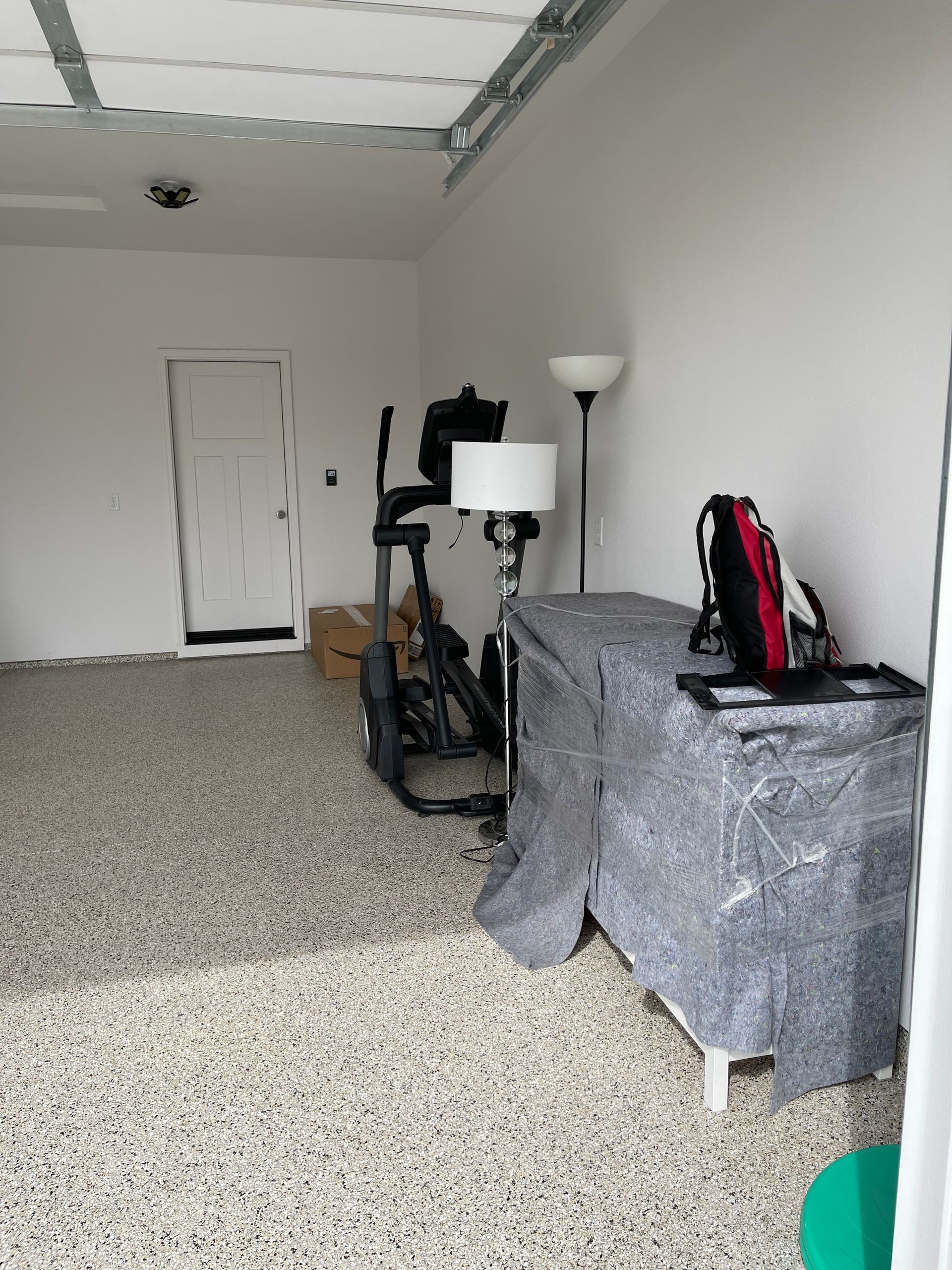 Garage with exercise equipment and covered storage; white walls, speckled floor.